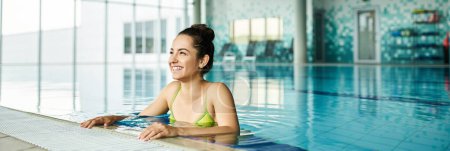 Téléchargez les photos : Une jeune femme brune dans un bikini vert vibrant se détend dans une piscine intérieure spa sereine. - en image libre de droit