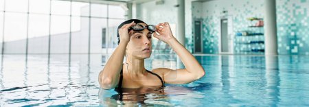A stylish young woman in a black bikini gracefully swims in an indoor spa pool.