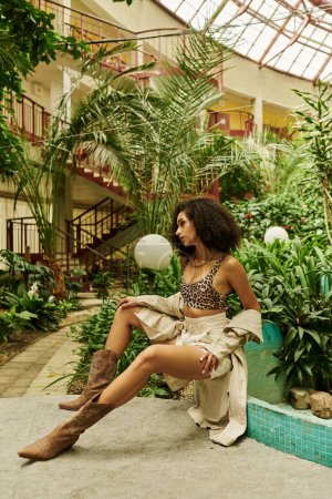full length of young black woman with curly hair posing in her trendy look in a botanical setting