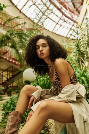 joven mujer afroamericana con el pelo rizado posando en su mirada de moda en un entorno botánico