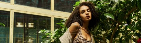 curly african american woman posing in her trendy look in exotic green setting with plants, banner