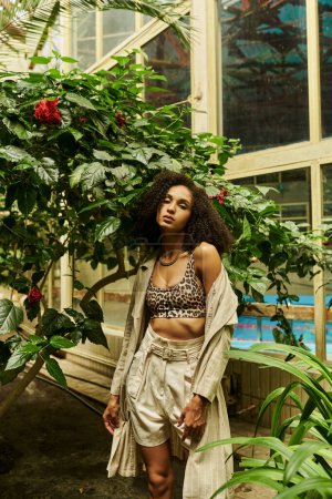 curly african american woman posing in her stylish look in exotic green setting with tropical plants