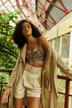Elegante mujer afroamericana con el pelo rizado posando en su aspecto de moda en el conservatorio tropical