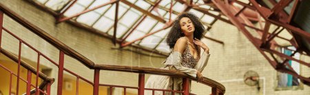 curly chic african american woman in animal print look posing against industrial backdrop, banner