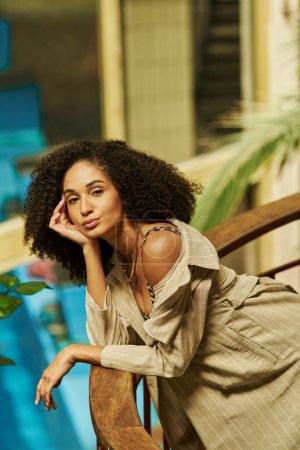 young african american woman with curly hair leaning on metallic structure in green garden setting