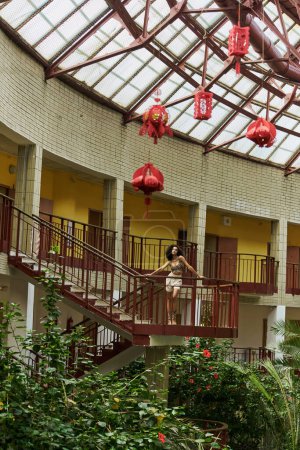 look from afar, curly young black woman in animal print, surrounded by greenery and red lanterns