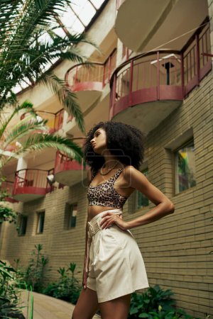 Confident black woman in chic style standing with hand on hip in atrium with botanical backdrop