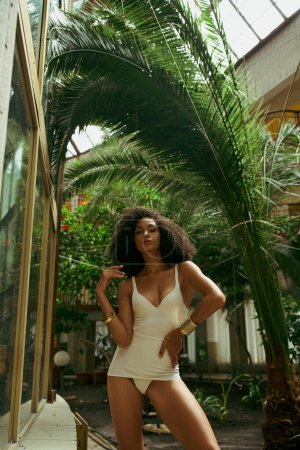 Retrato digno de Vogue de la joven africana americana rizada en un traje de baño, en medio de una exuberante vegetación