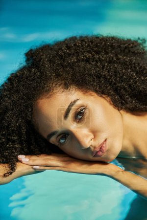 Porträt einer jungen afrikanisch-amerikanischen Frau mit lockigem Haar, die in die Kamera blickt und im Wasser schwimmt