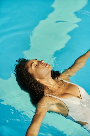 young african american woman with curly hair swimming in her bathing suit inside of pool