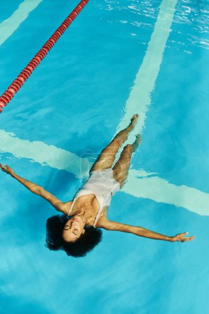 top view of young and curly african american woman swimming on back in clear pool water, serenity