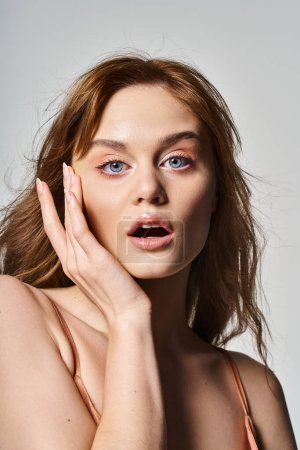 Schönheitsporträt einer überraschten Frau mit trendigem Make-up, die in die Kamera auf grauem Studiohintergrund blickt