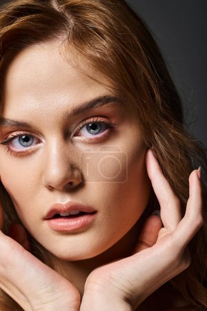 Closeup portrait of pretty woman with peach natural makeup touching face on grey background