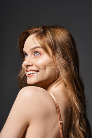 Téléchargez les photos : Portrait de la jeune femme souriante et joyeuse aux yeux bleus, posant sur fond gris foncé - en image libre de droit