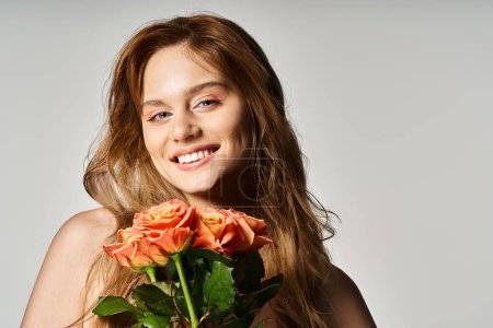 Porträt einer lächelnden jungen Frau mit blauen Augen, die pfirsichfarbene Rosen auf grauem Hintergrund hält