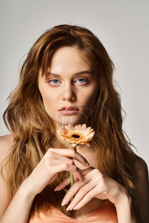 Beauty shot of pretty woman with blue eyes, with gerbera daisy near face on grey background