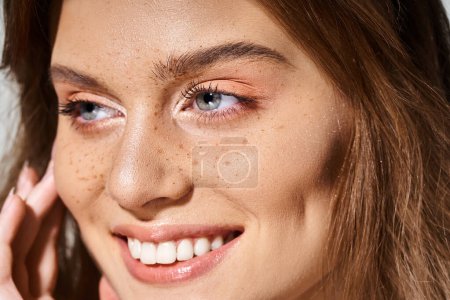 Foto de Primer plano retrato de belleza de mujer sonriente con maquillaje de melocotón y pecas sobre fondo gris - Imagen libre de derechos