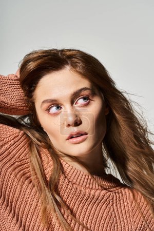 Portrait of curious woman looking up with natural makeup, wearing sweater, touching her hair