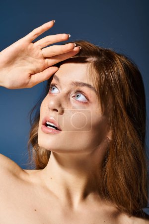 Neugierige Frau mit Pfirsich-Make-up und Sommersprossen, Stirn anfassen und auf blauem Hintergrund aufblicken