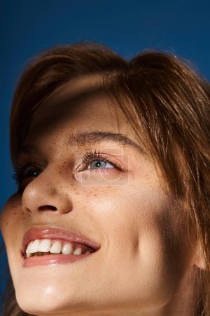 Primer plano retrato de belleza de mujer de ojos azules sonrientes con pecas sobre fondo azul oscuro