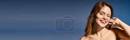 Smiling woman making funny winky face with tongue, touching her ear on dark blue background, banner