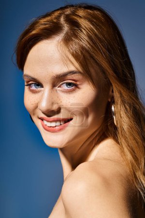 Foto de Vista lateral de chica sonriente con ojos azules, maquillaje desnudo melocotón con pecas sobre fondo azul - Imagen libre de derechos