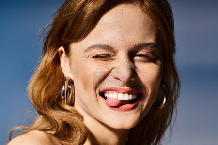 Foto de Primer plano de la mujer sonriente haciendo la cara guiñada divertida con la lengua, sobre fondo azul - Imagen libre de derechos