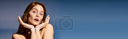 Schönheitsfoto einer überraschten jungen Frau mit blauen Augen und Händen nahe dem Kinn auf grauem Hintergrund, Banner