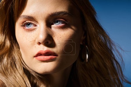 Closeup beauty photo of pretty woman with blue eyes, peach makeup and freckles on blue background