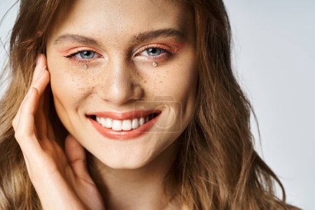 Closeup beauty portrait of smiling girl with tear face jewels, peach makeup and freckles