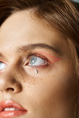 Closeup beauty portrait of woman eyes with tear shaped face jewels, peach makeup and freckles