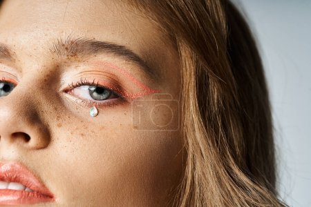 Closeup beauty portrait of woman eyes with peach makeup eyeliner, tear face jewels and freckles