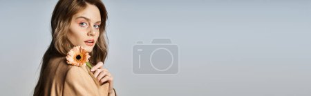 Mujer atractiva mirando a la cámara y sosteniendo la margarita, usando maquillaje de melocotón, joyas de la cara, pancarta