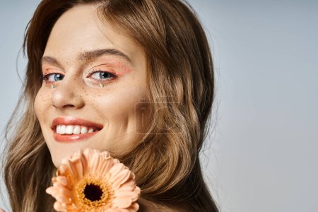 Closeup beauty shot of woman winking with peach makeup, gerbera daisy, face jewels and freckles