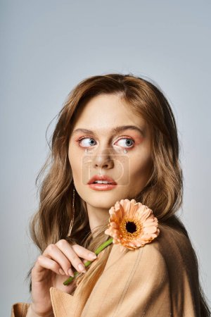 Attractive woman looking up and holding daisy, wearing peach makeup, face jewels