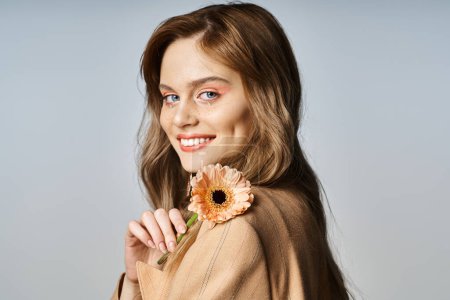 Attractive cheerful woman looking at camera and holding daisy, wearing peach makeup, face jewels