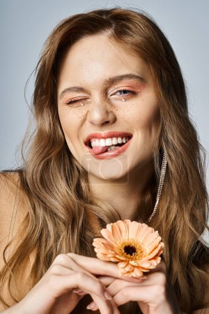 Photo for Winking cheerful woman looking at camera and holding daisy, wearing peach makeup, face jewels - Royalty Free Image