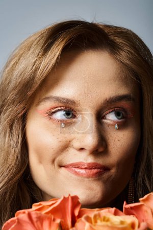 Foto de Primer plano de mujer sonriente con maquillaje de melocotón, joyas de la cara y pecas, sosteniendo rosas - Imagen libre de derechos