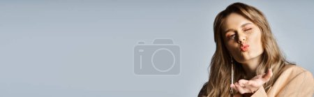 Téléchargez les photos : Femme gaie portant une veste beige, maquillage pêche et bijoux étincelants visage soufflant baiser, bannière - en image libre de droit