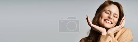 Téléchargez les photos : Heureuse femme joyeuse avec des bijoux de visage souriant à la caméra touchant le visage, sur fond gris, bannière - en image libre de droit