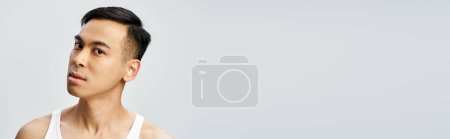 Téléchargez les photos : Bel asiatique homme en blanc débardeur posant dans gris studio réglage, bannière - en image libre de droit