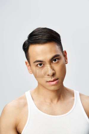 Handsome Asian man in a grey tank top confidently posing in a studio setting.