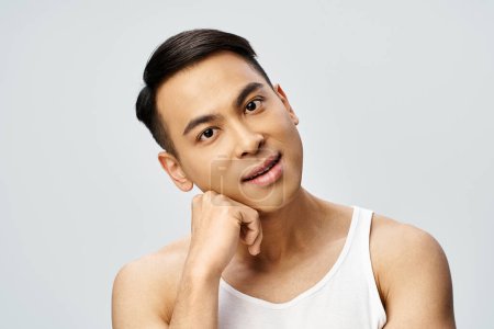 A handsome Asian man in a grey studio striking a pose while wearing a tank top.