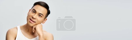 Téléchargez les photos : Beau asiatique homme frappant une pose dans un cadre de studio gris tout en portant un débardeur. - en image libre de droit