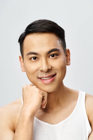 A handsome Asian man exudes joy with a beaming smile on his face in a gray studio setting.