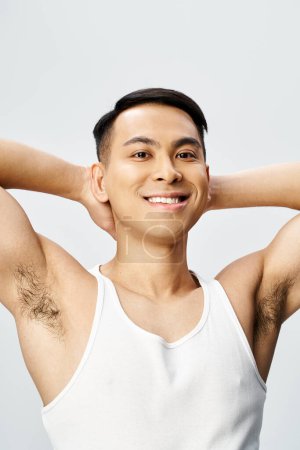 Foto de Un retrato de un hombre asiático guapo en una camiseta blanca con las manos detrás de la cabeza, exudando un comportamiento tranquilo y relajado. - Imagen libre de derechos