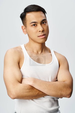 Un guapo asiático posa confiadamente con los brazos cruzados en un estudio gris.