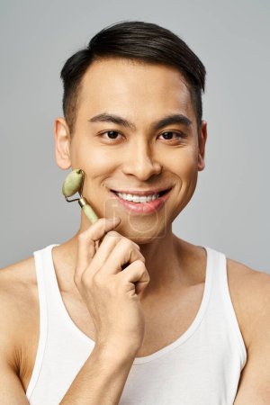 Handsome Asian man gently holding jade roller in his hand, showcasing serenity and smile
