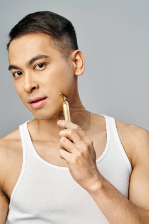 Asian man with a stylish appearance shaving in a grey studio setting.