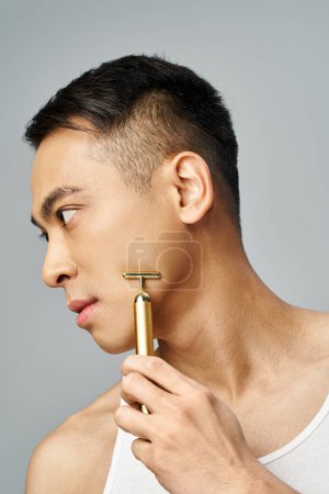 Hombre asiático guapo en estudio gris, sosteniendo una navaja de oro y mirando hacia otro lado